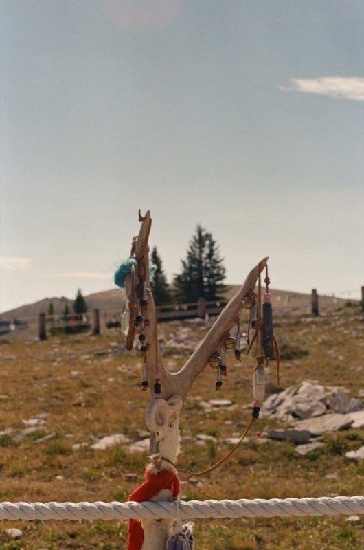 An antler lashed to a rope fence, hung with bells, beads and cloth.