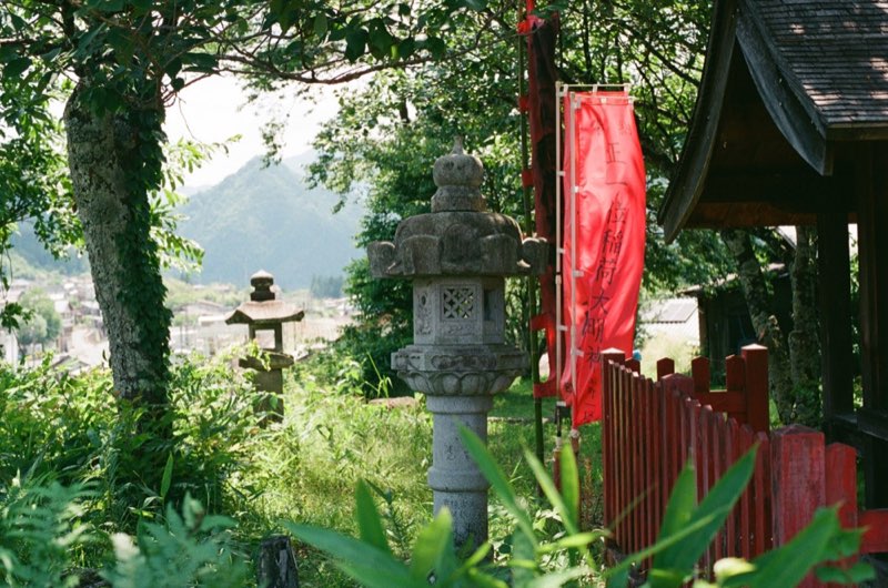 A hillside Inari shrine above a town, red banner and stone lanterns.