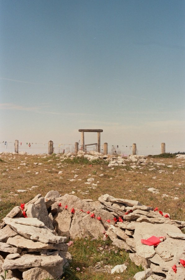 A cairn of flat stones strung with red rags, a wooden gate standing on the ridge behind it.